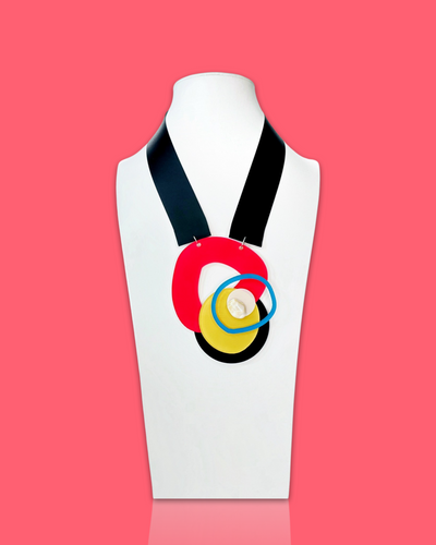 Abstract bold fashion necklace in magenta and peacock blue with intricate detailing on a white mannequin stand.