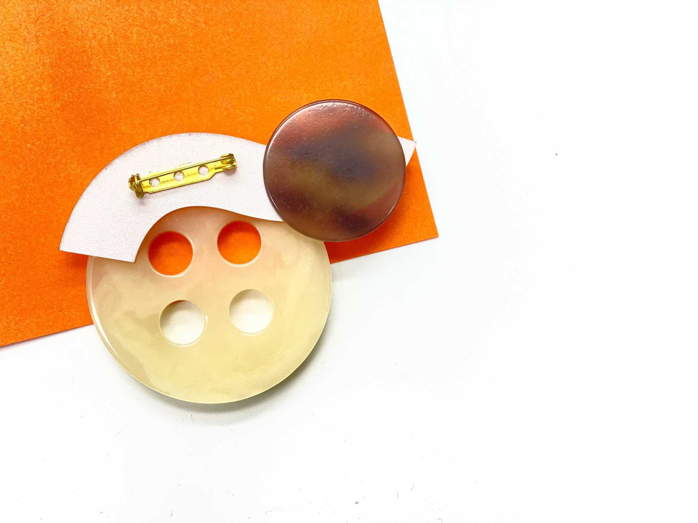 Bold button bar-pin brooch in tiger color with geometric design, featuring plastic beads and polymer clay, displayed on an orange background.